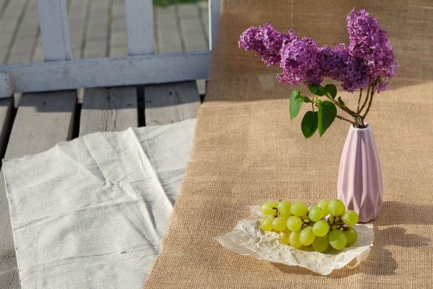 静物和食物照片。一串葡萄和插着紫丁香的花瓶放在木地板上的粗麻布上图片下载