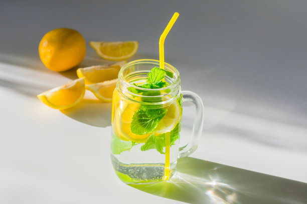 一张特写照片，一个杯子里装满了水、柠檬片和薄荷叶和黄色吸管，旁边是一片柠檬图片下载