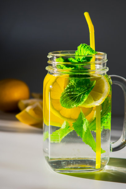 一个特写的垂直高对比度照片，一个杯子装满水，切片柠檬和薄荷叶与黄色吸管图片下载