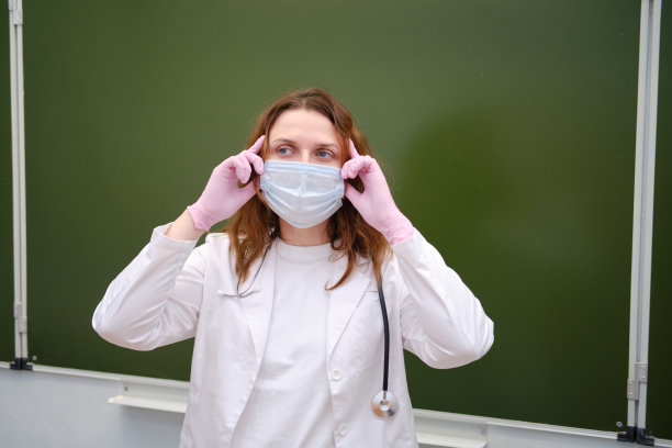 一位戴着医用口罩的校医用双手托着他的头图片下载