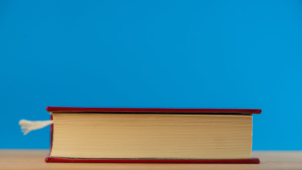 蓝色背景的橡木桌子上放着一本合上的书。图片下载