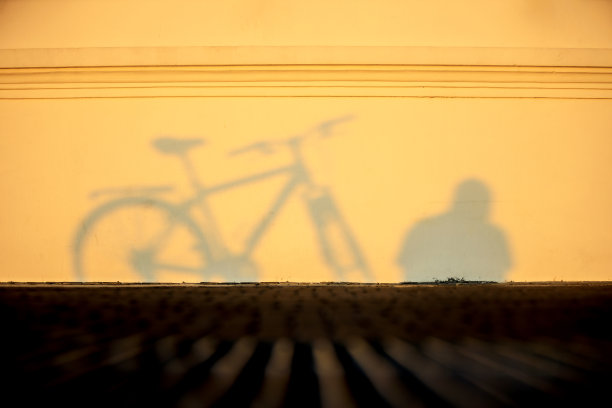 早晨骑车，自行车的影子映在墙上，阳光泛着温暖的黄色图片下载