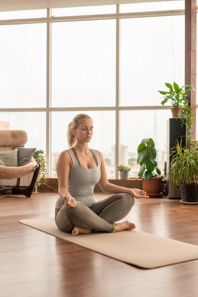 年轻而安详的女运动员交叉双腿，坐在垫子上摆莲花姿势图片下载