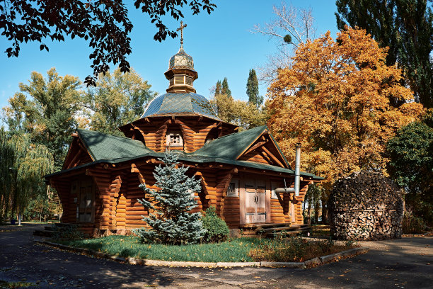 有金色圆顶和十字架的木制教堂。秋天的风景。在黄色的树叶的背景下收获了一片木柴。图片下载