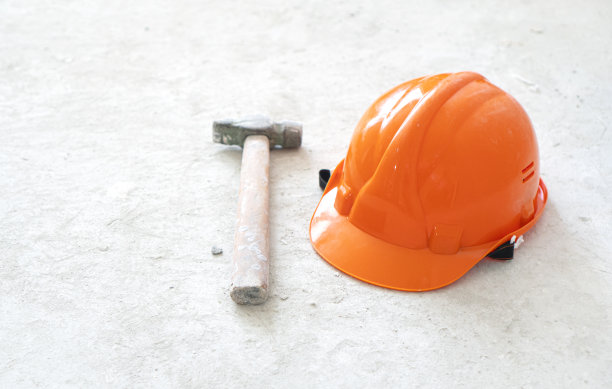 橙色的安全帽和混凝土背景上的锤子。图片下载