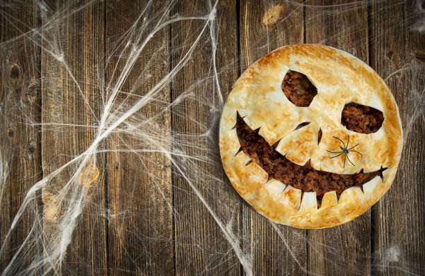 万圣节的食物。木制的桌子上放着自制的万圣节鬼脸肉馅饼。副本的空间。图片下载