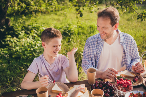 正面的小男孩的照片坐在桌子在户外玩新鲜的有机夏天午餐告诉说爸爸爸爸有趣的新闻吃三明治图片下载