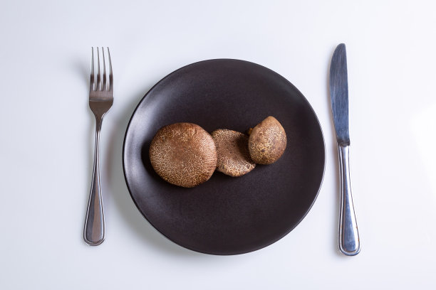 生泽西奶牛蘑菇在一个黑色的盘子和刀叉附近在一个白色的背景俯视图。水平方向。高质量的照片图片下载