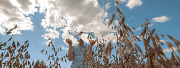 一个男孩站在麦田里，手里拿着两面镜子，镜子里的天空倒映在镜子里图片下载