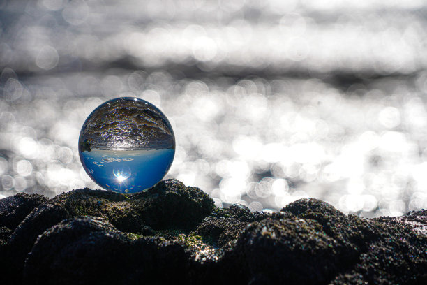 摄影水晶照片球显示颠倒的天空海滩和波浪平衡在岩石上的沙滩。图片下载