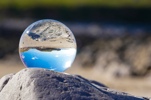 摄影水晶照片球显示颠倒的天空海滩和波浪平衡在岩石上的沙滩。图片下载