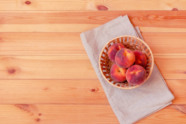 成熟的桃子装在柳条篮子里，放在木桌上。图片下载