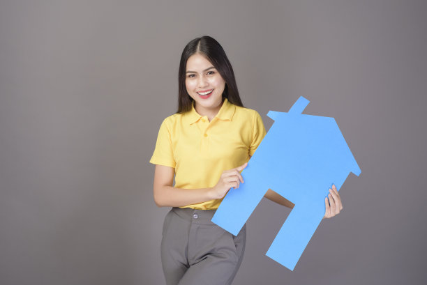 年轻自信美丽的女人穿着黄色的衬衫是举着一个家唱歌在灰色的背景工作室图片下载