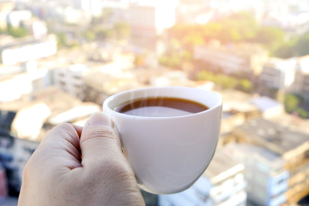 一个男人的手拿着热咖啡杯与烟雾在一个新的早晨在现代城市的背景图片下载