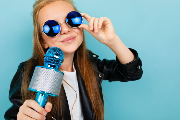 一个戴着墨镜微笑的欧洲女孩用一个浅蓝色背景的麦克风唱歌图片下载