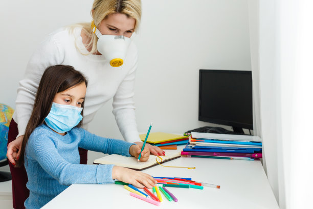 疫情隔离期间，戴防护口罩的母女在家保持距离辅导作业图片下载