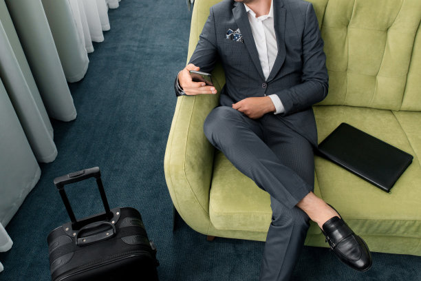 愉快的商人用电话坐在酒店房间里拿着手提箱出差图片下载