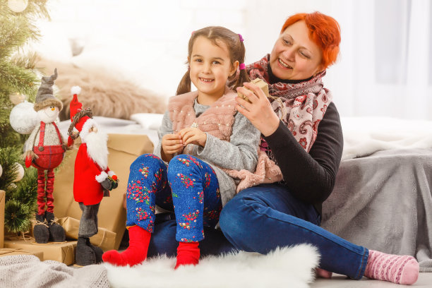 家庭、节日、世代与人的观念——微笑的女孩与祖母在家里装饰圣诞树图片下载