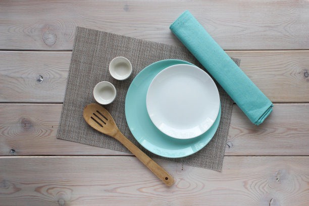 白色和绿松石色的盘子，木制的厨房勺子，灰褐色背衬上绿松石色的餐巾。木制背景上的盘子。图片下载