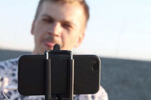 一名年轻人在水边用自拍杆和智能手机自拍图片下载