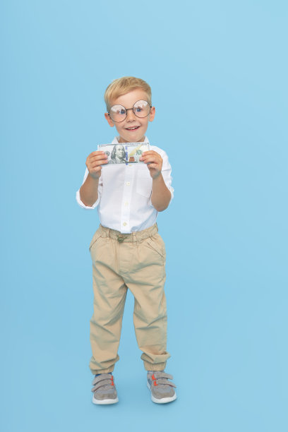 孩子和金钱。戴着眼镜、穿着白衬衫的聪明男孩拿着一张蓝色背景的纸币。儿童教育受益贷款的概念。图片下载