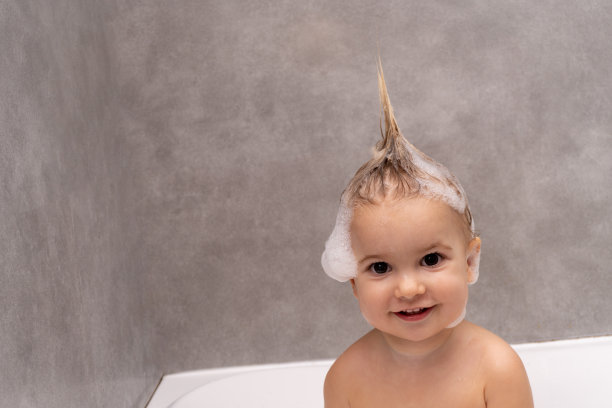 可爱的金发小女孩白种儿童在浴室洗澡泡沫的头和头发，灰色的背景，复制空间。图片下载