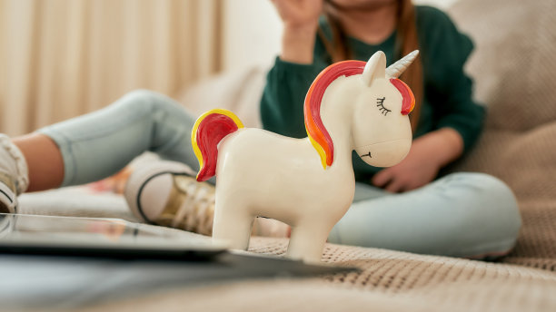 一个微笑的独角兽钱箱前的一个小女孩独自坐在一个明亮的房间的沙发上图片下载