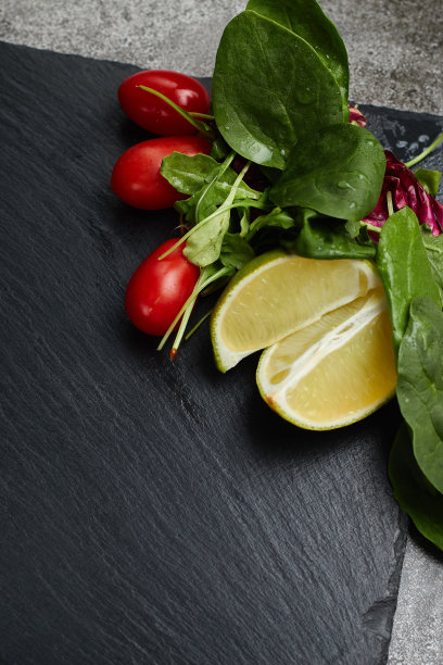 酸橙、生菜、绿色蔬菜和红色的樱桃番茄躺在深色石板背景上，文字空间，餐厅菜单图片下载