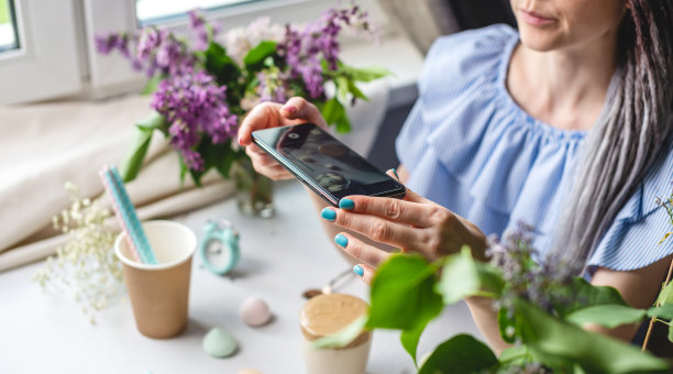 一名妇女正在用手机拍下一杯清晨的达尔戈纳咖啡。白色背景，柔和的颜色和淡紫色的花图片下载