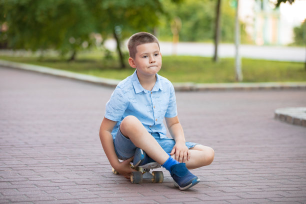 男孩坐在滑板上。街上一个七岁的男孩，一脸沉思图片下载