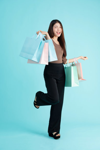 肖像的快乐年轻的亚洲年轻女子拿着购物袋在蓝色的背景。图片下载