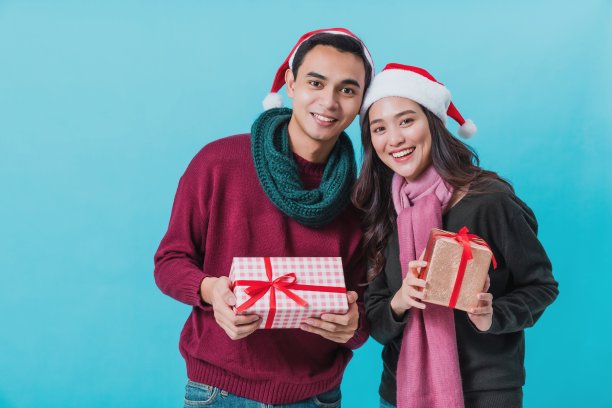 幸福的年轻亚洲夫妇拿着圣诞礼物盒与幸福的笑脸孤立在蓝色背景在工作室拍摄。圣诞节庆祝情人的概念。图片下载