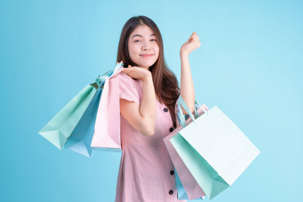 肖像的快乐年轻的黑发女人拿着信用卡和购物袋在蓝色的背景。购物狂概念图片下载