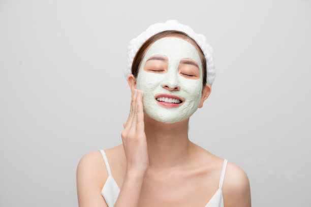 美丽的亚洲可爱的女孩与美丽的皮肤显示面膜霜在她的脸在白色的背景。图片下载