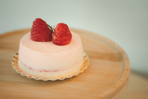 粉红色的慕斯蛋糕，上面覆盖着粉红色的奶油和浆果，放在一个圆形的木架上图片下载