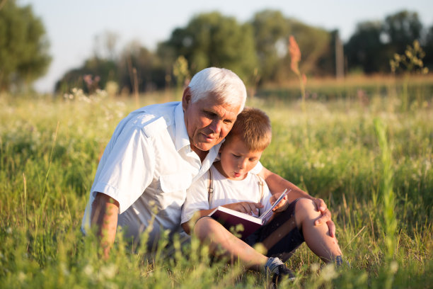 中景:爷爷和孙子在草地上一起看书。小男孩在阅读中迈出了第一步。图片下载