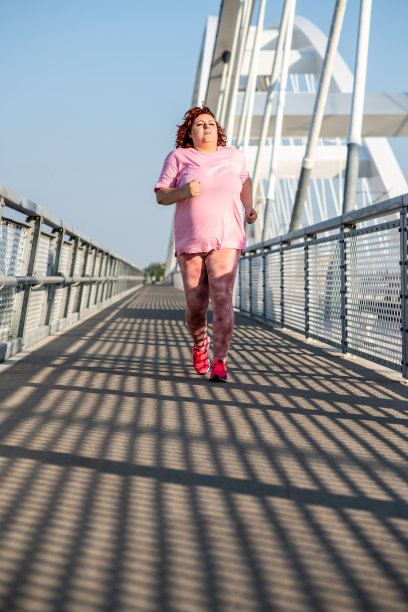 一个全身肥胖的女人在一个阳光明媚的日子在户外跑步。图片下载