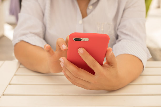 一个女人手里拿着一个整洁的指甲，手里拿着一个红色的手机盒在一个在线约会网站上写短信。特写照片图片下载