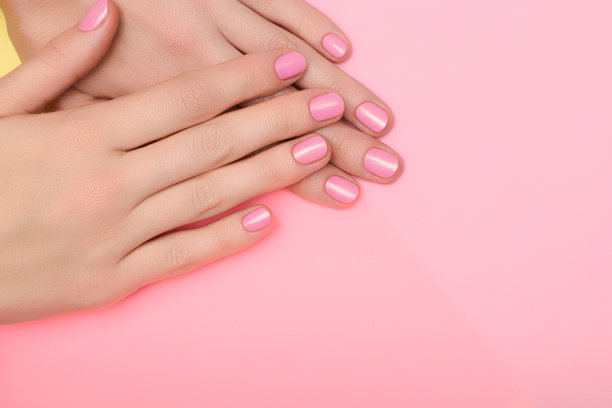 女性的手与粉红色的指甲设计。粉色指甲油，美甲。女性的手在粉红色的背景上。图片下载