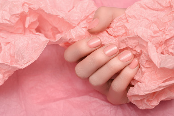女性的手有浅粉色的指甲设计。淡粉色指甲油修剪过的手。女人的手拿着淡粉色的皱巴巴的纸图片下载
