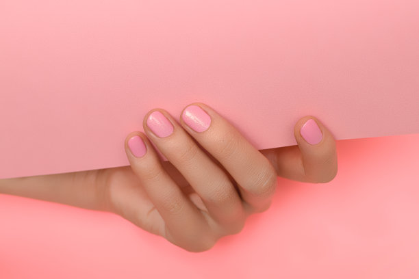 美丽的女性手与完美的粉红色指甲油持有粉红色的纸在粉红色的背景图片下载