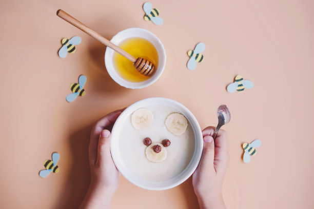 给孩子们的有趣早餐。小熊造型的婴儿粥，背景是香蕉、蜂蜜和蜜蜂。婴儿食品菜单。图片下载