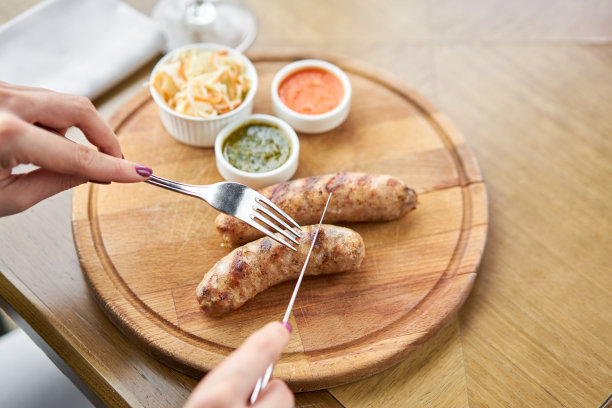 餐厅午餐，一位女士正在切烤香肠。在木板上工作烧烤餐厅的菜单，一系列不同肉类的照片。酸菜和两种酱汁图片下载