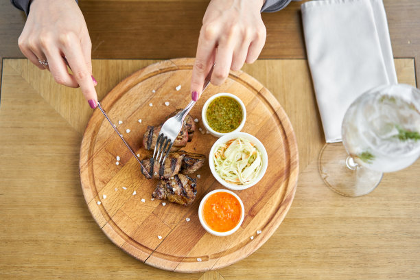 在一家餐馆的午餐中，一位女士在烤架上切着一块块的肝。在木板上工作烧烤餐厅的菜单，一系列不同肉类的照片。图片下载