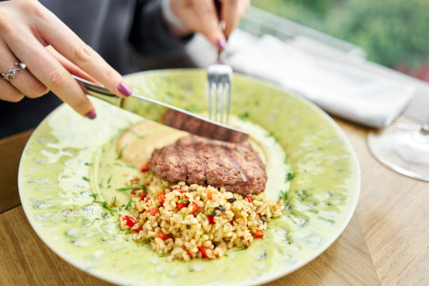 在一家餐馆的午餐，一位女士正在切美味的牛排，配上碎干干的干洋葱和熏洋葱奶油。烧烤餐厅的菜单，一系列不同肉类的照片图片下载