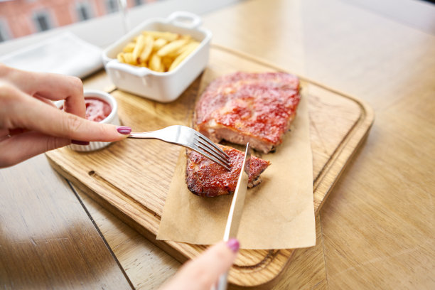 在餐厅吃午饭，一位女士切美味的排骨。全排肋排，木盘烧烤，配炸薯条和沙拉图片下载