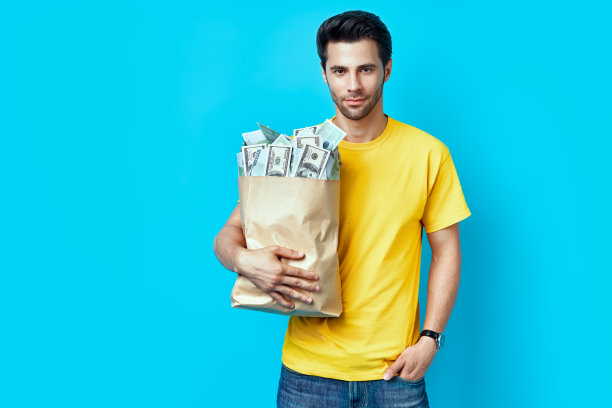 英俊的男人拿着纸袋装满了钱孤立在蓝色背景图片下载