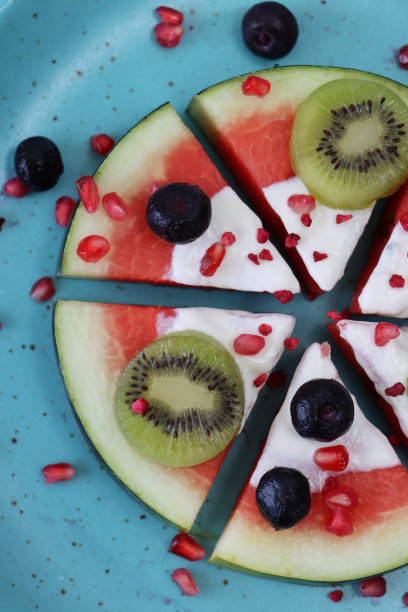 全框特写图像斑点，蓝绿色的盘子，切片西瓜披萨，水果沙拉披萨设计的西瓜片顶部与酸奶，猕猴桃，蓝莓和石榴籽，高架视图图片下载