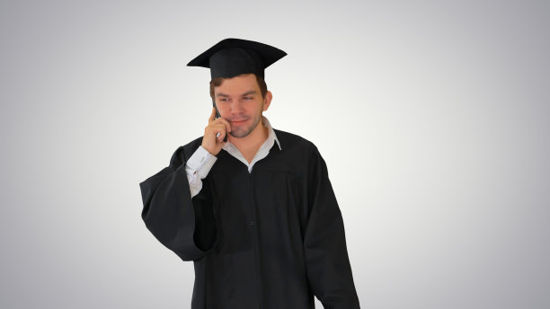 穿着学士服的男毕业生一边讲着电话图片下载