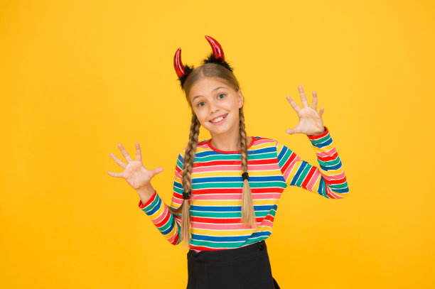 她的恶魔。万圣节派对女孩黄色背景。小女孩戴着红魔鬼的角发带。神秘的万圣节女孩。小女孩变成了邪恶的恶魔图片下载